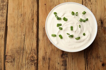 Tasty sour cream with green onions in bowl on wooden table, top view. Space for text