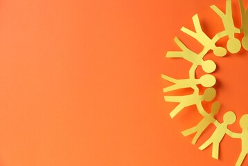 Paper figures of people holding hands on orange background, top view. Space for text