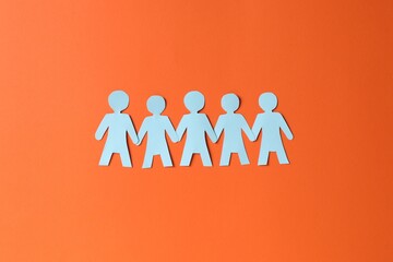 Paper figures of people holding hands on orange background, top view