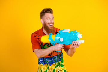 Energetic young man enjoying summer fun with a water gun against a vibrant yellow background