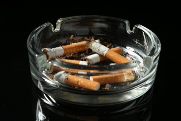 Cigarette butts in ashtray on black background, closeup