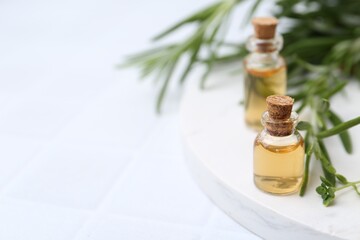 Bottles of essential oil and herbs on white tiled table, closeup. Space for text