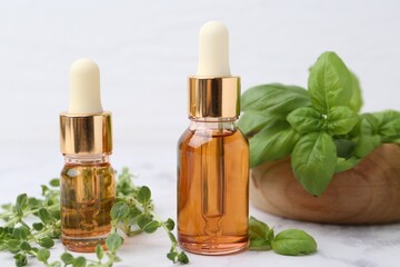 Bottles of essential oil and herbs on white marble table, closeup