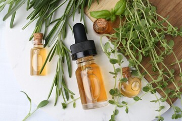 Bottles of essential oil and herbs on white table, flat lay