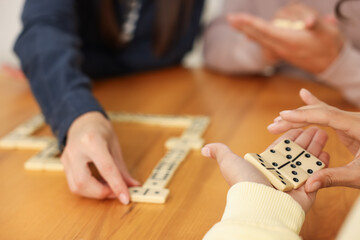 Friends playing dominoes at wooden table, closeup