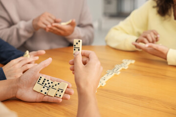 Friends playing dominoes at wooden table indoors, closeup