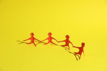 Human paper figures holding hands on yellow background