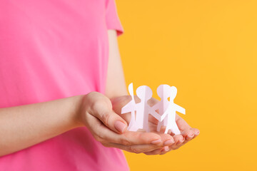 Woman holding paper figures of people on orange background, closeup