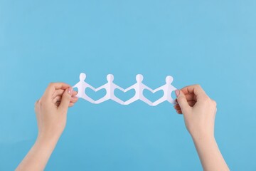 Woman holding paper figures of people on light blue background, closeup
