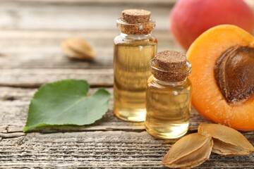 Bottles of essential oil, fresh apricots, kernels and green leaf on wooden table, closeup. Space...