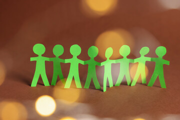 Paper figures of people holding hands on brown background, bokeh effect