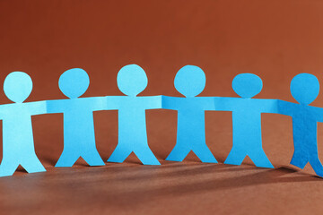 Paper figures of people holding hands on brown background, closeup