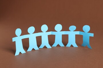 Paper figures of people holding hands on brown background