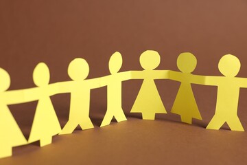 Paper figures of people holding hands on brown background, closeup