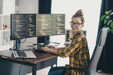 Young female programmer coding software at workspace with multiple screens showcasing dynamic...