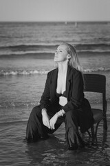 Girl in a black business suit in the sea on the beach on a wooden retro chair. Photo model....