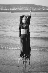 Girl in a black business suit in the sea on the beach on a wooden retro chair. Photo model....
