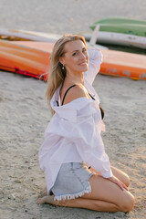 Blonde girl in a white shirt in the sea on the beach in the summer at sunset