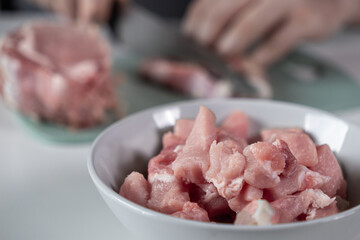 White bowl filled with raw diced pork meat, freshly prepared by hands for home cooking, highlighting healthy meal preparation and culinary activity