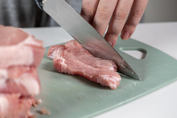 A close-up of a hand using a sharp kitchen knife to slice raw fresh meat on a green cutting board, symbolizing home cooking, meal preparation, and healthy diet choices