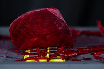 Vibrant red peeled beet being freshly grated on a mandoline, creating colorful shredded pieces, symbolizing healthy eating and nutritious natural ingredients