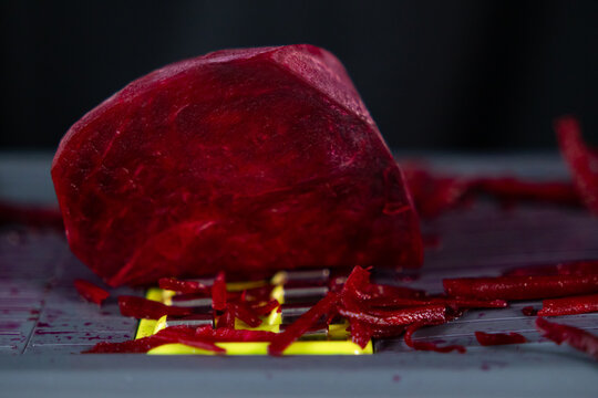 Vibrant red peeled beet being freshly grated on a mandoline, creating colorful shredded pieces, symbolizing healthy eating and nutritious natural ingredients