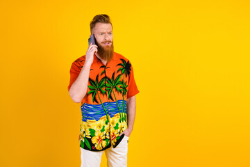 Young bearded man in colorful tropical shirt speaking on mobile phone against bright yellow...