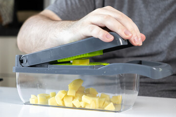 Man operating a kitchen vegetable chopper, efficiently dicing potatoes for home cooking,...
