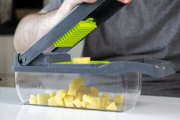 Person's hand operates a sleek gray and green vegetable dicer, efficiently cutting fresh potatoes...