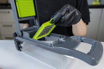 Person in black gloves meticulously assembling a multi-functional modern kitchen vegetable chopper,...