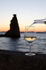 A person pours a glass of Albariño wine with the tower of San Sadurniño in the background. Silhouette at sunset.