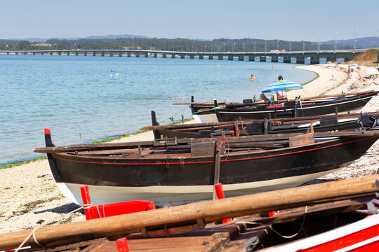 Wooden dornas on O Bao beach in Arousa Island. Traditional boats. Access bridge to Arousa Island.