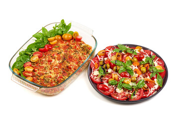 Tomato basil bake in glass dish and caprese salad on black plate, isolated on white background.