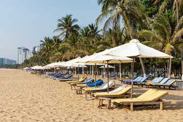 A row of sun loungers with umbrellas, palm trees and white sand tropical beach in the resort town of Nha Trang, located on the South China Sea in Vietnam, Asia. Popular travel tropical destination
