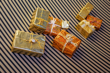 A multitude of gift boxes wrapped in gold foil lie on a striped blanket.