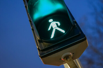 A pedestrian traffic light photographed from a low angle with a green man on the lamp and the...