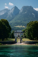 Obraz premium A magnificent estate stands proudly at the water's edge, framed by lush green trees and majestic mountains under a clear blue sky. The tranquil scene invites exploration and relaxation