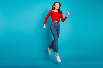 Excited young woman jumps in stylish casual outfit against vibrant blue background showcasing...