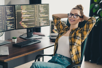 Young female programmer relaxing in her workspace with dual monitors displaying code, enjoying a...