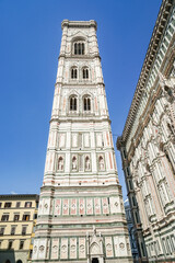 A tall building of Florence Cathedral with a clock tower and a blue sky in the background