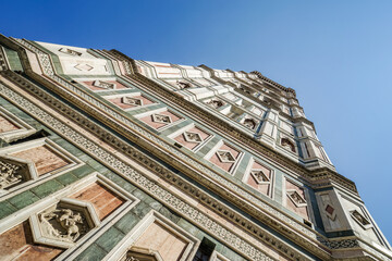 A tall building of Florence Cathedral with a clock tower and a blue sky in the background