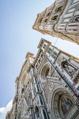 A tall building of Florence Cathedral with a clock tower and a blue sky in the background