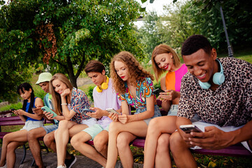 Buddies sitting on a park bench using smartphones and sharing moments together on a bright summer...