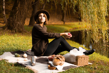 Golden hour at a fall picnic — a woman enjoys a crisp apple while sitting near a serene lake...