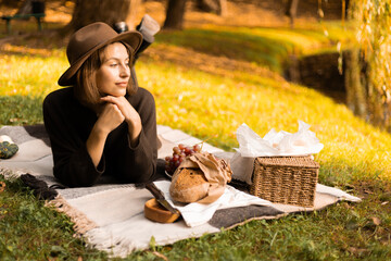 Afternoon sunlight illuminates a peaceful picnic scene as a woman lounges with a basket of seasonal...
