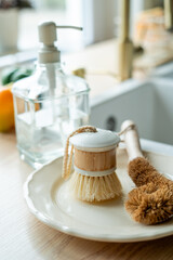 Plate with an ecobrush for washing dishes near the sink, soap in a glass bottle, a towel.