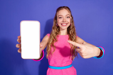 Joyful young woman in pink dress highlights smartphone display on vibrant purple backdrop with...