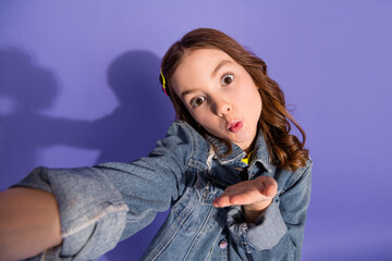 Smiling young girl in denim jacket posing playfully with hand gesture against a vibrant purple backdrop