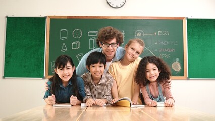 Caucasian professional teacher sitting while hugging diverse cute student at class and looking at...