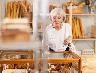 Woman in casual clothes chooses fresh croissants for breakfast in bakery